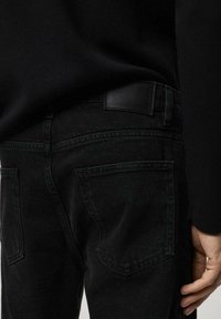 Jeans de mezclilla negra con un corte ajustado, que presentan bolsillos traseros, una etiqueta de cuero en la cintura y detalles de costura sutiles.