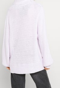 Vaaleanvioletti ylisuurikokoinen neulepaita, jossa on resorit helmassa ja hihansuissa sekä teksturoitu, avoin neulospitsi.