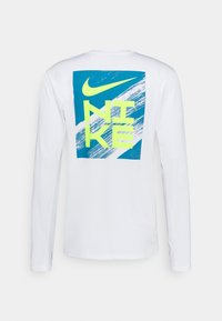 Pitkähihainen valkoinen paita, jossa on sininen ja neonkeltaisen graafinen kuva, jossa on teksti "NIKE" siveltimenvedon kuviolta.