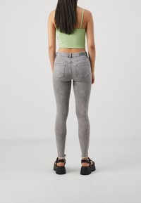 Grå slim jeans med hög midja, med en slitna fåll och två bakfickor, i kombination med en grön crop top och kraftiga svarta sandaler.
