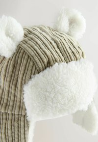 Chapeau en gabardine avec doublure en peluche blanche. Présente des oreilles d'ours et des rayures en velours côtelé beige texturé. Les rabats d'oreilles doublés s'étendent vers le bas.