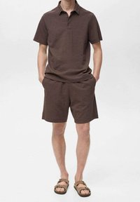 Polo shirt beige texturé et shorts assortis avec une coupe décontractée et des coutures plates. Porté avec des sandales marron ajustables.