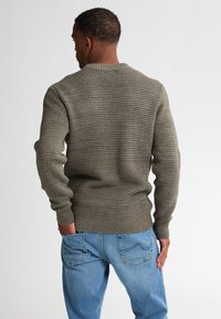 Khaki textuur trui met een ronde hals, geribbelde manchetten en zoom, gecombineerd met lichtblauwe spijkerbroek. De trui heeft een wafelbreipatroon.