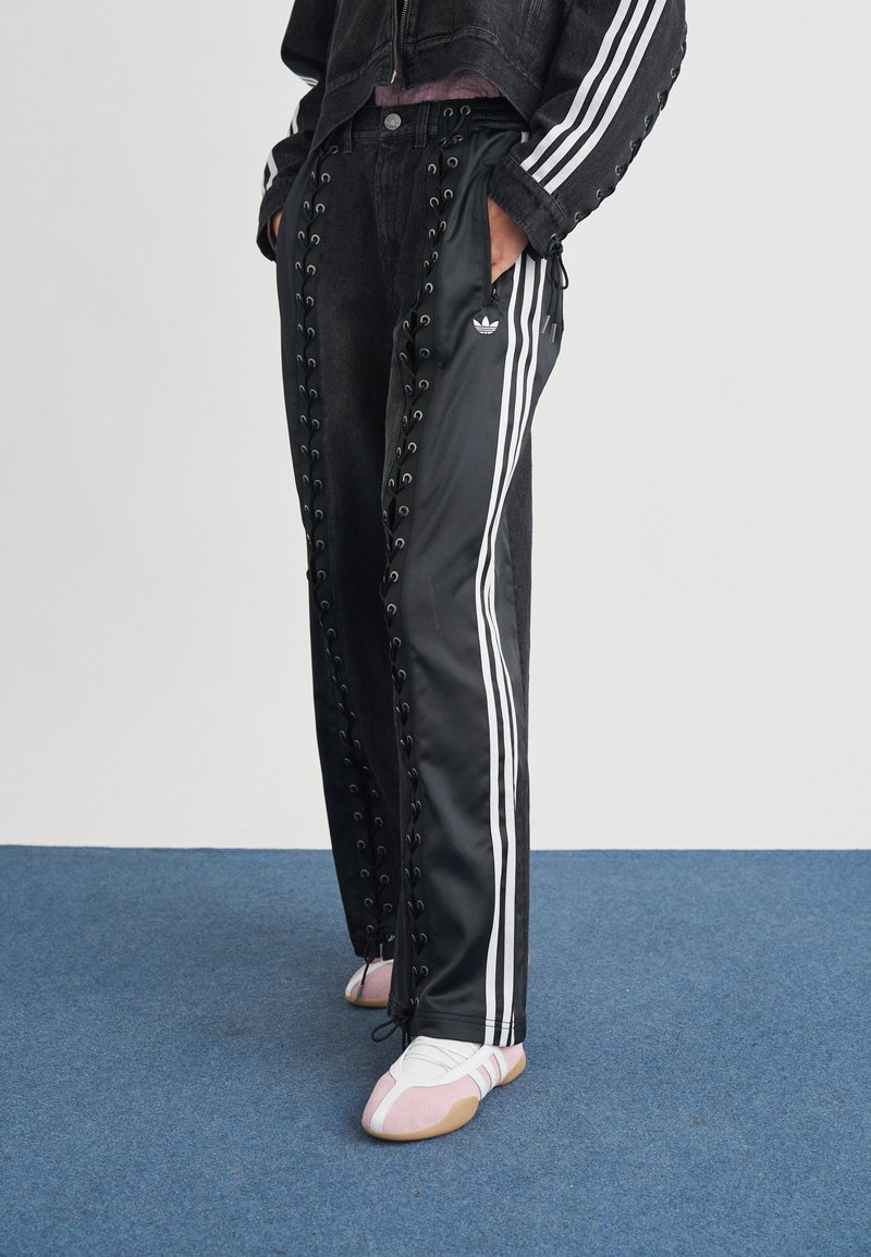 Μαύρο παντελόνι φόρμας με λευκές ρίγες στο πλάι, διακοσμημένο με κορδόνια στις πλευρές. Συνδυασμένο με λευκά και ροζ αθλητικά παπούτσια.