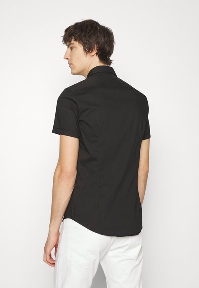 Chemise noire à manches courtes avec un col classique, texture lisse et coupe ajustée, dotée de coutures dorsales pour une silhouette structurée.