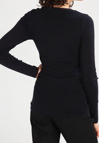 Schwarzes Langarmoberteil mit figurbetonter Silhouette, aus einem weichen Stoff, mit Rundhalsausschnitt und glatter Textur.