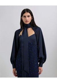 Vestido de satén azul marino con un corsé ajustado y mangas abullonadas. Lunares texturizados adornan la falda. Presenta una lazada en el cuello.