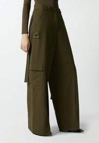 Hlače širokih nogavica od maslinasto zelene tkanine, s bočnim terenskim džepovima, elegantnim zatvaračem i akcentima od srebrne boje. Glatka tekstura.