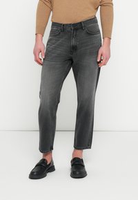 Grijze jeans met rechte pijpen, een verweerde finish, vijf zakken en lichte slijtage bij de zoom, gecombineerd met zwarte loafers.