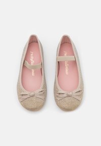 Ballerine beige realizzate in tessuto texturizzato, dotate di un fiocco anteriore, una fascia elastica e solette rosa con la scritta "Pretty Ballerinas" stampata in oro.