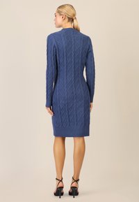 Abito maglione blu a maglia con maniche lunghe, polsini e orlo a costine. Tessuto liscio, forma aderente, taglio fino al ginocchio. Tacchi neri a fascia.