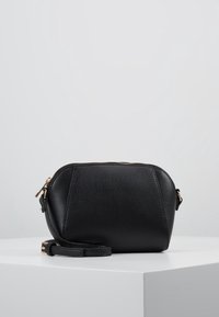 Svart läderväska med strukturerad yta, rund form, guldfärgad hårdvara och avtagbar rem. Dragkedjestängning på toppen.