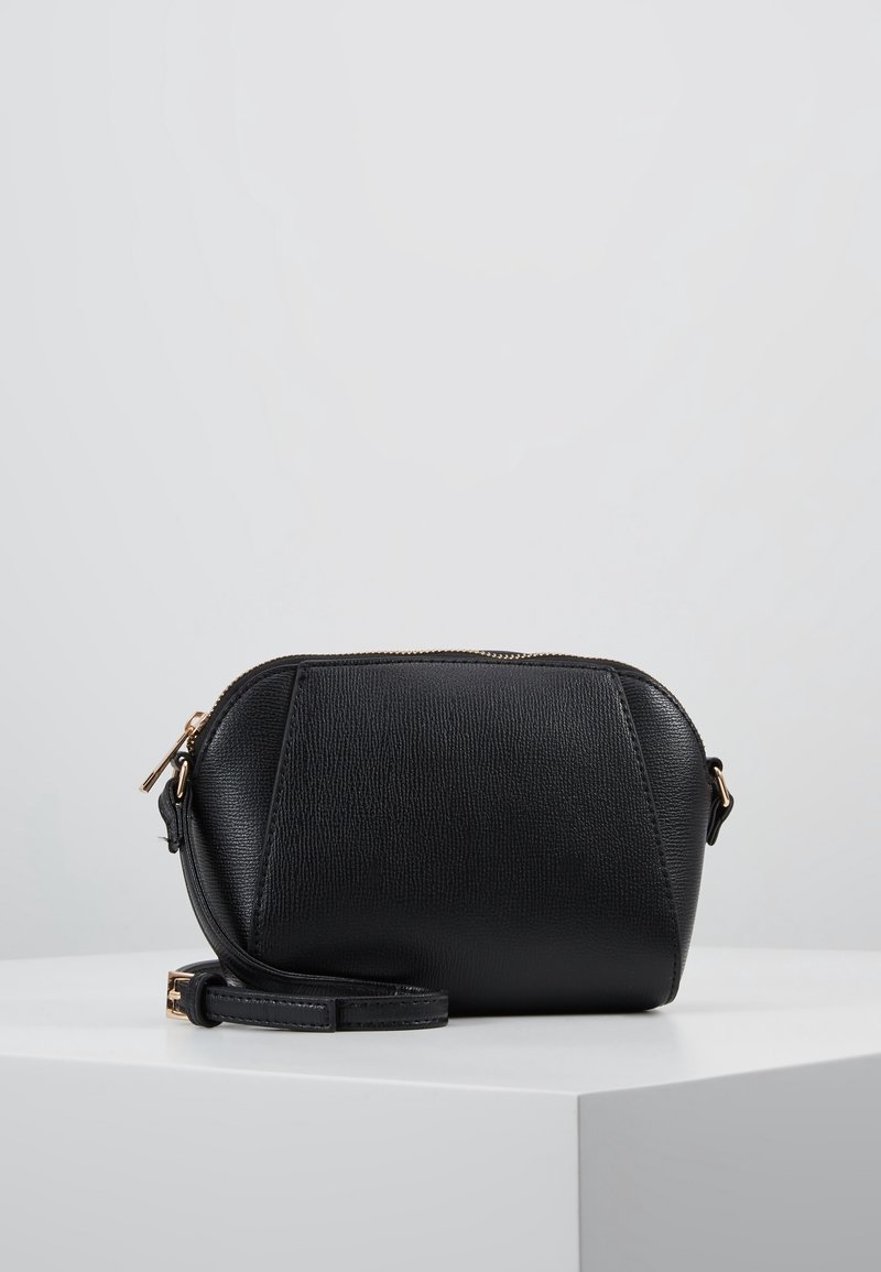 Svart läderväska med strukturerad yta, rund form, guldfärgad hårdvara och avtagbar rem. Dragkedjestängning på toppen.