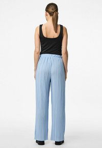 Ljusblå plisserade vida byxor med elastisk midja, tillsammans med en svart ärmlös topp. Tyget verkar mjukt och flödande.