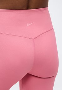 Κοντινό πλάνο ενός ατόμου που φοράει ροζ Nike κολάν με ψηλή μέση, δείχνοντας την πλάτη και τις λεπτομέρειες των ραφών.