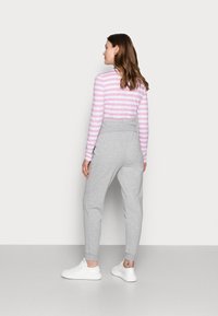 Grå joggebukser med elastisk liv, kombinert med en rosa og hvitstripet langermet skjorte og hvite sneakers.