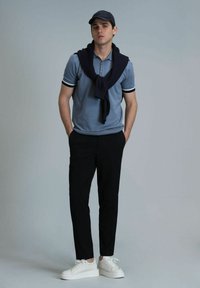 Polo bleu clair avec des accents noirs et blancs, pull marine noué autour des épaules, pantalon noir et baskets blanches.