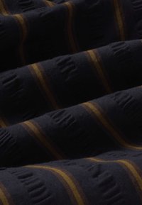 Tissu foncé avec un texte en relief subtil et des rayures verticales marron, présentant des plis doux et des détails de texture.