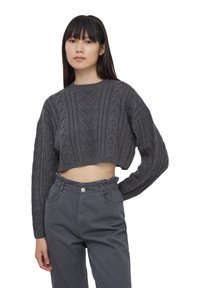 Maglione grigio corto in maglia con motivo a treccia e maniche lunghe, abbinato a pantaloni grigi a vita alta con elastico in vita e tasche.