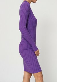 Robe violette côtelée avec des manches longues, un col rond et une coupe ajustée, mettant en valeur la texture et les rayures verticales.