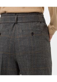 Pantalon à carreaux gris avec un tissu texturé, comportant des motifs orange et noir, deux poches arrière et des boutons en guise d'ornements.