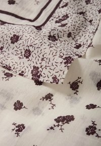 Tissu blanc avec de petits motifs floraux bordeaux foncé et des accents éparpillés. Matière légère et texturée avec un bord replié.
