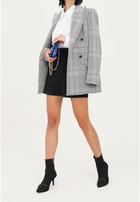 Blazer doppiopetto grigio a quadri sopra una camicia bianca, abbinato a pantaloni corti neri e stivaletti neri con tacco. Pochette blu con dettaglio a catena.
