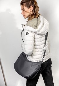 Borsa a tracolla nera con texture liscia e design curvo, indossata da una persona con un giubbotto puffer bianco su uno sfondo chiaro.