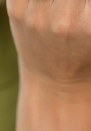 Gros plan d'une main à la peau claire et lisse, montrant des textures subtiles et de fines lignes sur le poignet, sur un fond neutre flou.