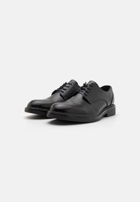 Chaussures habillées en cuir noir avec une finition lisse, bout rond et semelle en caoutchouc plate. Présente trois œillets pour les lacets et un design minimaliste.