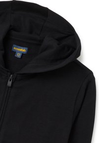 Sudadera con cremallera negra, fabricada con un material suave, capucha ajustable y una etiqueta azul que dice "essentials" en texto amarillo.
