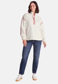 White fleece pullover with a half-zip, pink accent stripes, soft texture, and two front pockets. Paired with blue jeans and white shoes.