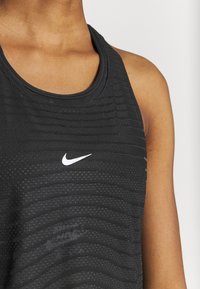 Černý sportovní tílko s texturovanou tkaninou a horizontálními pruhy, na přední straně s malým bílým logem Nike.