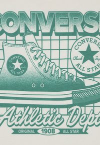 Πράσινο γραφικό ενός αθλητικού παπουτσιού Converse σε ανοιχτό φόντο, με υφασμάτινο σχέδιο, εμβληματικό λογότυπο και κείμενο "Athletic Dept.".