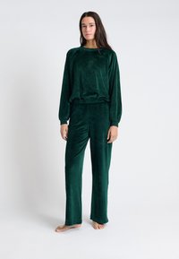 Groene velours loungewear set met een losse lange mouw top en wijde pijpen. Eenvoudig ontwerp met een zachte textuur en zonder zichtbare hardware.