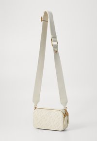 Witte schoudertas met een textuurpatroon van het logo, gouden hardware en een stevige canvas schouderriem. Rechthoekige vorm met ritsluiting.