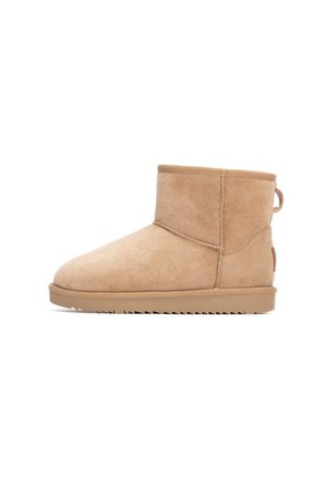 Botas de tobillo de ante marrón claro con puntera redondeada, superficie texturizada y suela de goma plana con surcos en zigzag. Detalle de tira en la parte trasera.