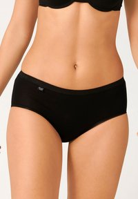 Culotte nera in cotone con una texture liscia, caratterizzata da un bordo a scallop e un piccolo etichetta con logo sul lato. Design classico a vita bassa.