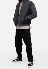 Black and gray padded jacket with zip closure, ribbed cuffs, and side pockets, paired with a gray sweatshirt, black pants, and black sneakers.