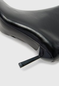 Gros plan sur une chaussure à talon aiguille en cuir noir, mettant l'accent sur le talon pointu et la texture lisse de la tige.