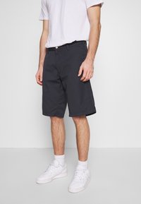 Mörkblå shorts i bomullsmaterial med en blandning av tyger, med rak front, bälteshällor och en lätt glans. Bärs med vita sportskor.