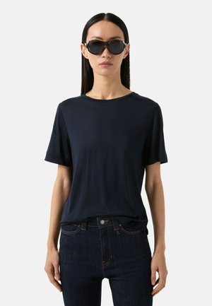 Navy blue short-sleeve t-shirt made of soft fabric, paired with high-waisted dark jeans. Model wearing round black sunglasses.