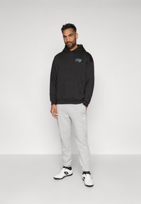 Mustmust musta, millel on ees tasku ja helesinine "Linn" tekst, on kombineeritud hallide treeningpükste ja valgete tossudega, millel on mustad aktsendid.