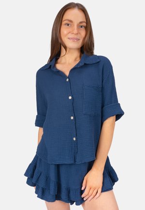 Chemise boutonnée en coton texturé bleu marine avec des manches retroussées et une poche poitrine, assortie d'une jupe froncée.