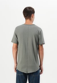 Graues Baumwoll-T-Shirt mit kurzen Ärmeln, einem runden Halsausschnitt und einem Rückennähten-Detail. Der Saum ist hinten etwas länger.