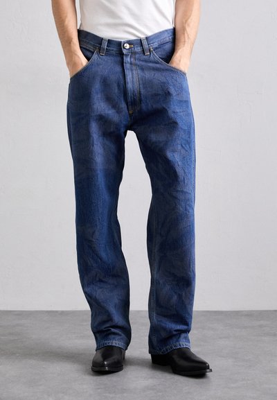 Modré džíny z denimu se straight střihem, designem s pěti kapsami, zapínáním na knoflík a kontrastním šitím. Nosené s jednoduchým bílým tričkem.