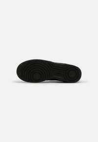 Svart sneakersula med strukturerad gummi, försedd med cirkulära mönster och en central logotyp. Platt design, robust konstruktion.