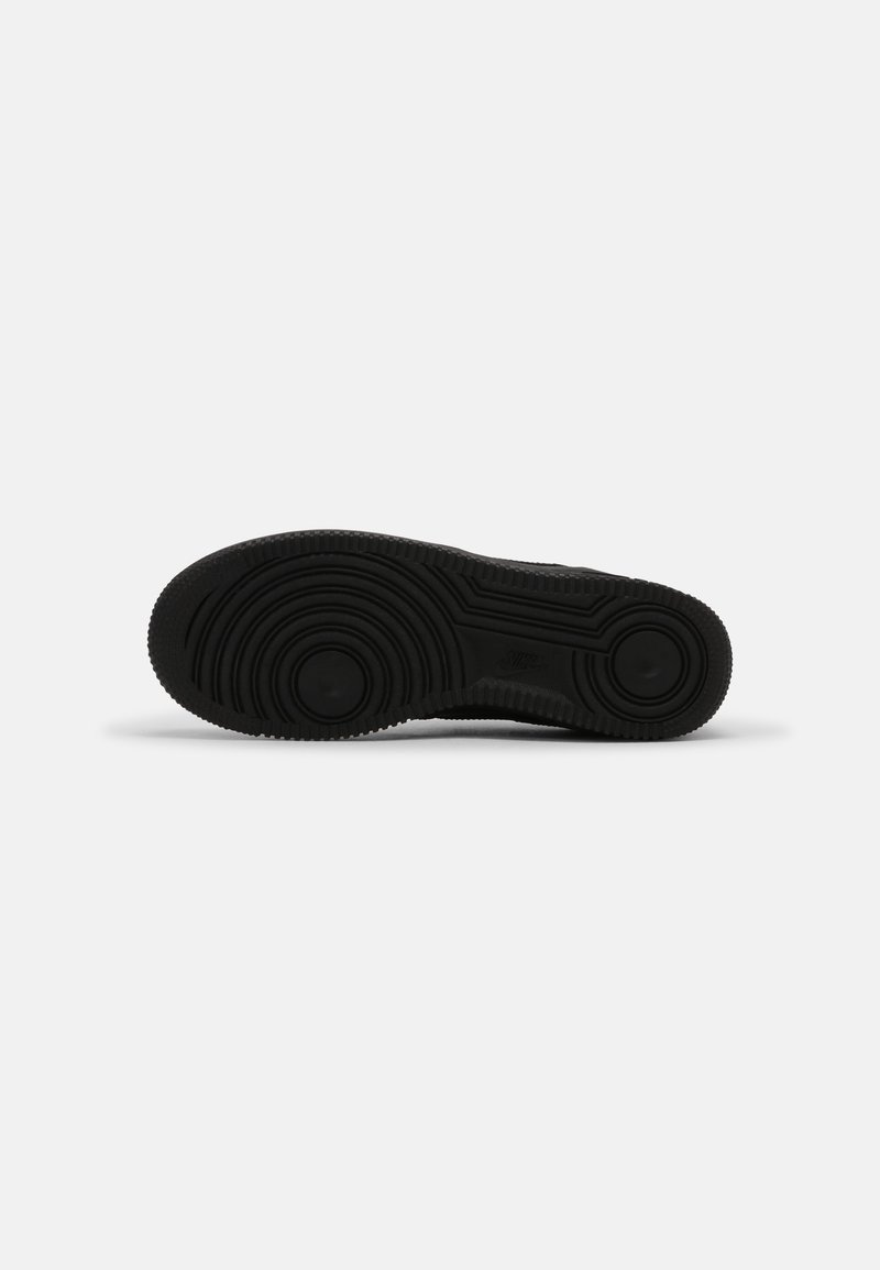 Semelle de sneaker noire en caoutchouc texturé, présentant des motifs de semelle circulaires et un logo central. Design plat, construction robuste.