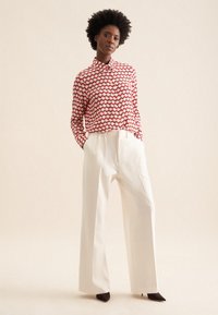 Camicia button-up a motivi rosso e bianco abbinata a pantaloni bianchi a gamba larga e tacchi a punta marroni. Tessuto morbido e vestibilità sartoriale.