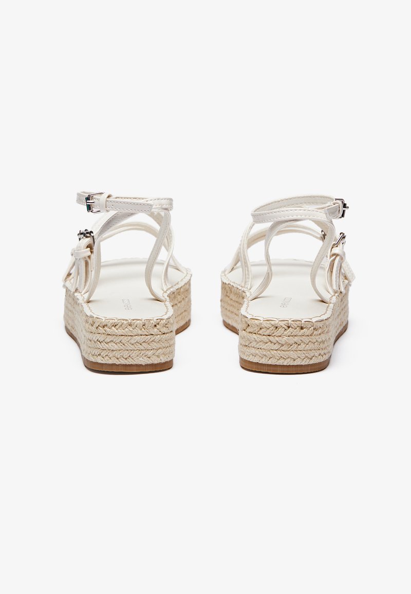 Sandalias de esparto blancas con suelas de plataforma de yute trenzado, que presentan tiras finas y hebillas ajustables en el tobillo, mostrando un diseño minimalista.